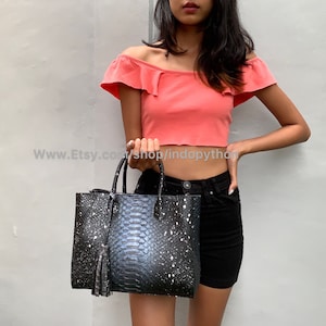 Może przedstawiać: Czarno-biała torba typu tote ze skóry węża z srebrnym frędzlem. Torba ma wzór białej farby w sprayu.