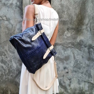 May include: A blue python leather backpack with a cream-colored strap and buckle closures. The bag is worn by a person in a white dress. The text "www.etsy.com/shop/IndoPython" is visible in the image.