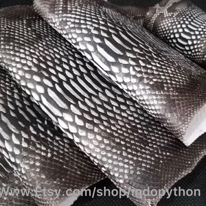 Może przedstawiać: Cztery kawałki czarnej i srebrnej sk&oacute;ry pytona, ułożone jeden na drugim. Sk&oacute;ra ma fakturowany wz&oacute;r.