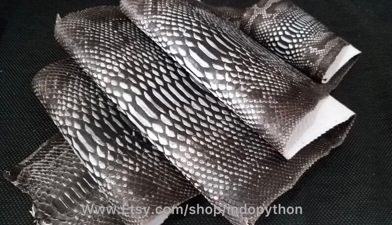 Może przedstawiać: Cztery kawałki czarnej i srebrnej sk&oacute;ry pytona, ułożone jeden na drugim. Sk&oacute;ra ma fakturowany wz&oacute;r.