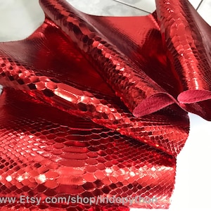 Op de afbeelding: Rood metallic slangenleer met een textuurpatroon. Het leer is gevouwen en toont het glanzende oppervlak.