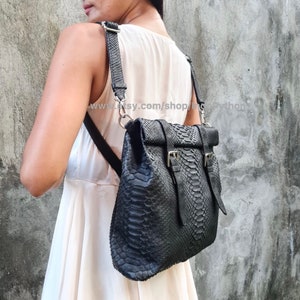 Peut inclure: Un sac &agrave; dos en cuir noir avec un motif en peau de serpent et des boucles argent&eacute;es. Le sac &agrave; dos a une fermeture &agrave; rabat et des bretelles r&eacute;glables.