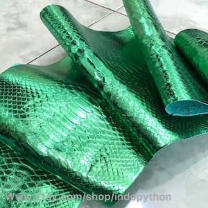 May include: Green metallic snakeskin-embossed leather fabric. The fabric has a shiny, reflective finish.