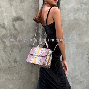 May include: A small, pink, yellow, and white snakeskin handbag with a silver chain strap and a silver top handle.
