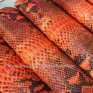 Op de afbeelding: Vier stukken oranje en zwarte pythonskin, op elkaar gestapeld. De huid heeft een textuurpatroon.