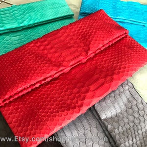 Peut inclure: Plusieurs pochettes de soir&eacute;e color&eacute;es, textur&eacute;es, avec un motif d'&eacute;cailles de reptile. Les couleurs incluent le rouge, le turquoise, le bleu sarcelle et le gris. Elles ont une fermeture pli&eacute;e de style enveloppe. L'image pr&eacute;sente la vari&eacute;t&eacute; de couleurs.
