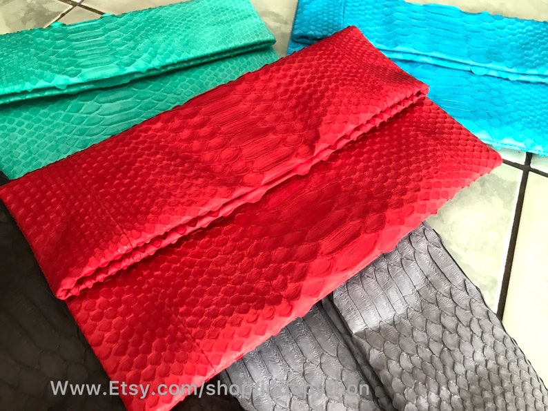 Peut inclure: Plusieurs pochettes de soir&eacute;e color&eacute;es, textur&eacute;es, avec un motif d'&eacute;cailles de reptile. Les couleurs incluent le rouge, le turquoise, le bleu sarcelle et le gris. Elles ont une fermeture pli&eacute;e de style enveloppe. L'image pr&eacute;sente la vari&eacute;t&eacute; de couleurs.