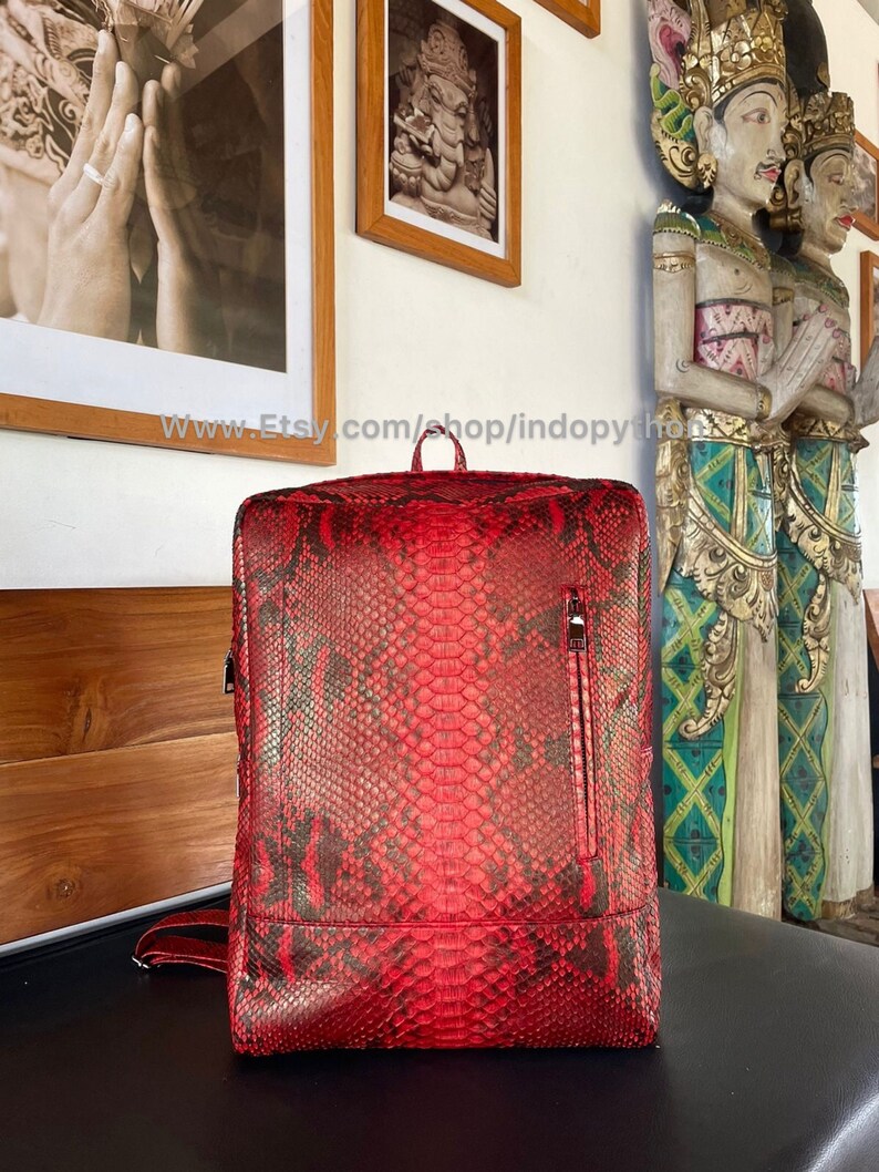 May include: A red snakeskin backpack with a zippered pocket on the front. The backpack is made of genuine python skin and has a unique, textured pattern.