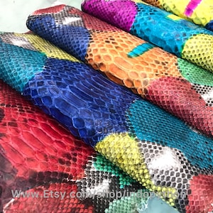 May include: A stack of colorful, patterned snakeskin leather hides. The hides are arranged in a rainbow pattern, with each hide featuring a different color and pattern. The hides are all cut into rectangular shapes and are ready to be used for crafting.