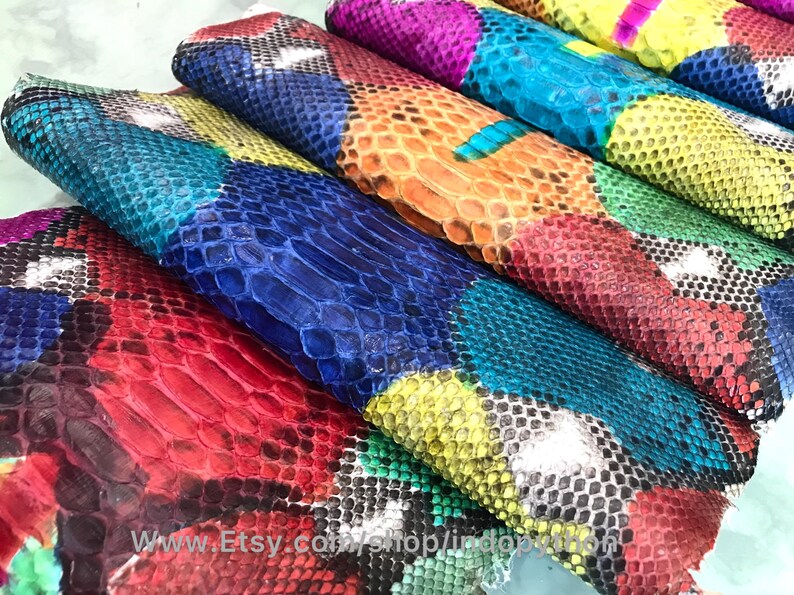 May include: A stack of colorful, patterned snakeskin leather hides. The hides are arranged in a rainbow pattern, with each hide featuring a different color and pattern. The hides are all cut into rectangular shapes and are ready to be used for crafting.