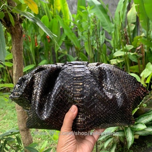 K&ouml;nnte beinhalten: Eine schwarze Clutch mit einem goldenen Schlangenhautmuster. Die Clutch ist aus echtem Leder und hat ein einzigartiges, strukturiertes Design.