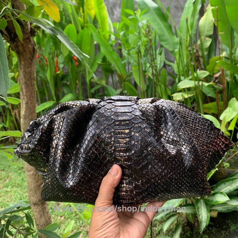 K&ouml;nnte beinhalten: Eine schwarze Clutch mit einem goldenen Schlangenhautmuster. Die Clutch ist aus echtem Leder und hat ein einzigartiges, strukturiertes Design.