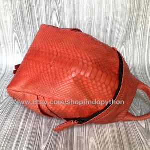 Pu&ograve; includere: Uno zaino in pelle di pitone arancione brillante con chiusura a zip e manico superiore. Lo zaino &egrave; realizzato in vera pelle di pitone e ha un aspetto testurizzato unico.