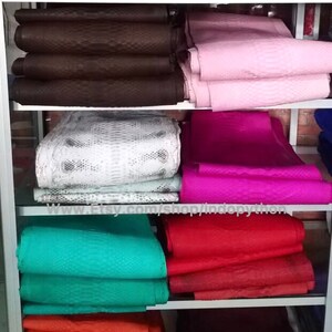 Może przedstawiać: P&oacute;łka z r&oacute;żnymi kolorami sk&oacute;r pytona. Sk&oacute;ry są ułożone na p&oacute;łkach w sklepie detalicznym. Sk&oacute;ry są dostępne w r&oacute;żnych kolorach, w tym czerwonym, r&oacute;żowym, turkusowym, białym i brązowym. Adres strony internetowej www.Etsy.com/shop/indopython jest widoczny na p&oacute;łce.