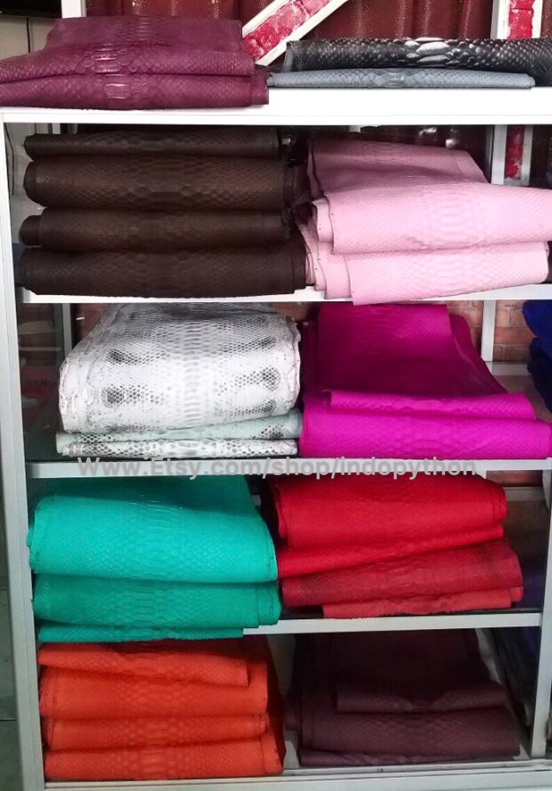 Może przedstawiać: P&oacute;łka z r&oacute;żnymi kolorami sk&oacute;r pytona. Sk&oacute;ry są ułożone na p&oacute;łkach w sklepie detalicznym. Sk&oacute;ry są dostępne w r&oacute;żnych kolorach, w tym czerwonym, r&oacute;żowym, turkusowym, białym i brązowym. Adres strony internetowej www.Etsy.com/shop/indopython jest widoczny na p&oacute;łce.