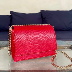 May include: A red snakeskin crossbody bag with a gold chain strap. The bag has a flap closure and a textured snakeskin pattern.