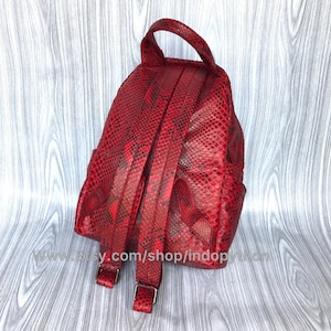 May include: Red snakeskin leather backpack with adjustable straps. The backpack has a small, compact design.