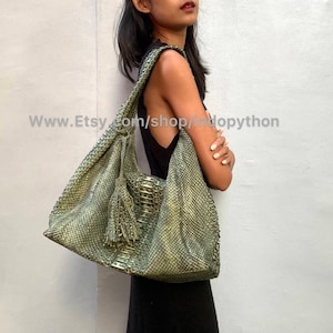 May include: A green snakeskin-textured hobo bag with a tassel. The bag has a long strap and is worn over the shoulder.