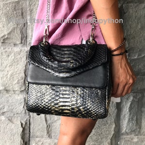 May include: A black and gold snakeskin handbag with a silver chain strap. The bag has a flap closure and a top handle.