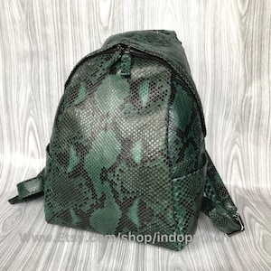 Może przedstawiać: Zielony plecak ze skóry węża z zamkiem błyskawicznym. Plecak ma małą kieszeń z przodu i regulowane paski.