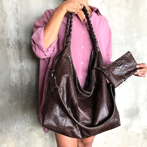 May include: A large brown leather tote bag with a braided strap and a smaller matching clutch. The bag has a snakeskin pattern.