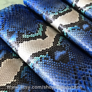 以下が含まれることがあります： 青、グレー、黒のパイソンレザーのクローズアップ。レザーはテクスチャのあるパターンで、何層にも折り畳まれています。画像の下部に「www.Etsy.com/shop/tokyo python」というテキストが表示されています。