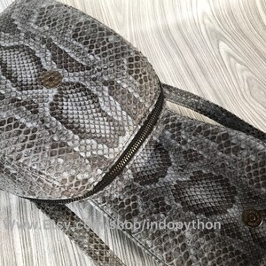 K&ouml;nnte beinhalten: Ein grauer Schlangenleder-Rucksack mit Rei&szlig;verschluss und einem Metall-Akzent. Die Tasche hat ein strukturiertes Schlangenledermuster.