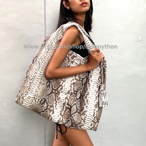 May include: A large, white and brown snakeskin tote bag with a long tassel. The bag is worn over the shoulder of a person.