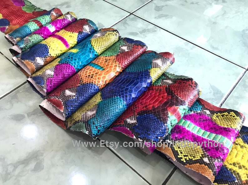 May include: A stack of colorful python skin hides, each piece featuring a unique pattern of scales. The hides are arranged in a rainbow of colors, including red, blue, green, yellow, and pink.