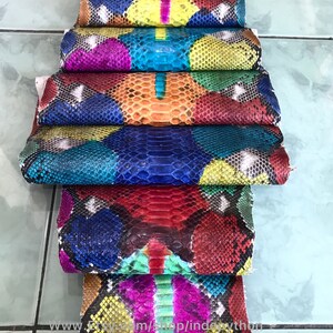 May include: A stack of colorful python skin hides, each piece featuring a unique pattern of scales and vibrant colors. The hides are arranged in a staggered pattern, showcasing the intricate details of the snake skin.