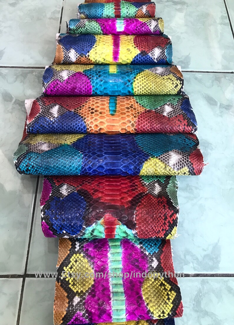 May include: A stack of colorful python skin hides, each piece featuring a unique pattern of scales and vibrant colors. The hides are arranged in a staggered pattern, showcasing the intricate details of the snake skin.
