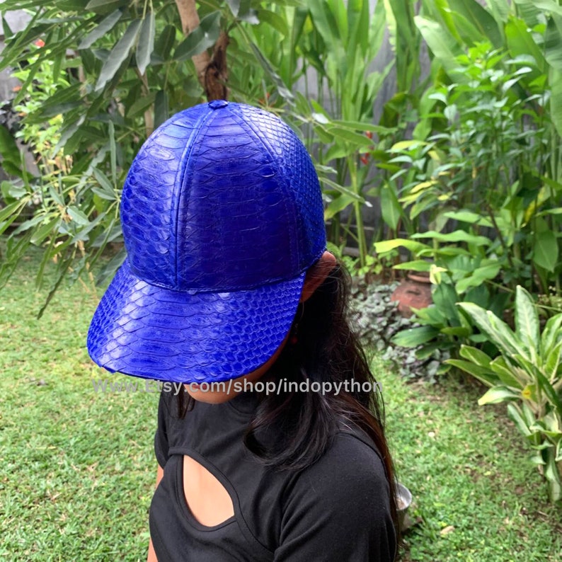 May include: A bright blue baseball cap made of python leather. The cap has a curved brim and a structured crown.