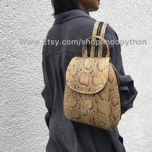 May include: A small, tan snakeskin backpack with black straps. The backpack has a flap closure and a zippered pocket on the front. www.Etsy.com/shop/mdopython