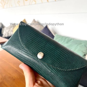 Op de afbeelding: Een donkergroene, getextureerde brillenkoker met een zilveren knoopsluiting. De koker heeft een klepsluiting en een gestikte rand. De Etsy shop URL is zichtbaar op de afbeelding.