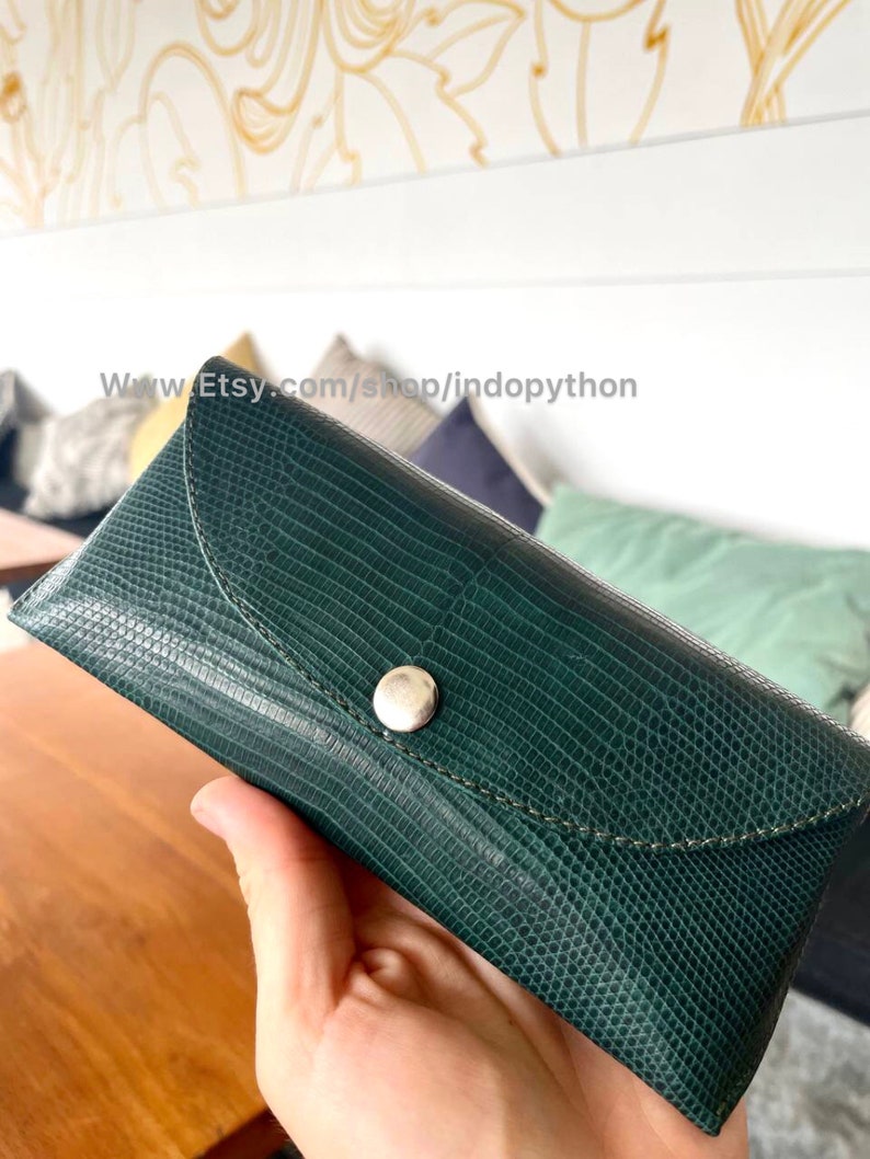 Op de afbeelding: Een donkergroene, getextureerde brillenkoker met een zilveren knoopsluiting. De koker heeft een klepsluiting en een gestikte rand. De Etsy shop URL is zichtbaar op de afbeelding.