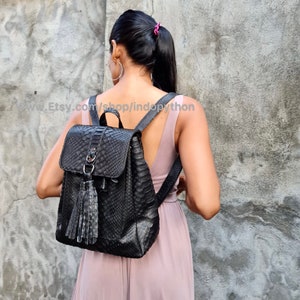 May include: A black leather backpack with a snakeskin pattern and a tassel. The backpack has a zip closure and adjustable straps.