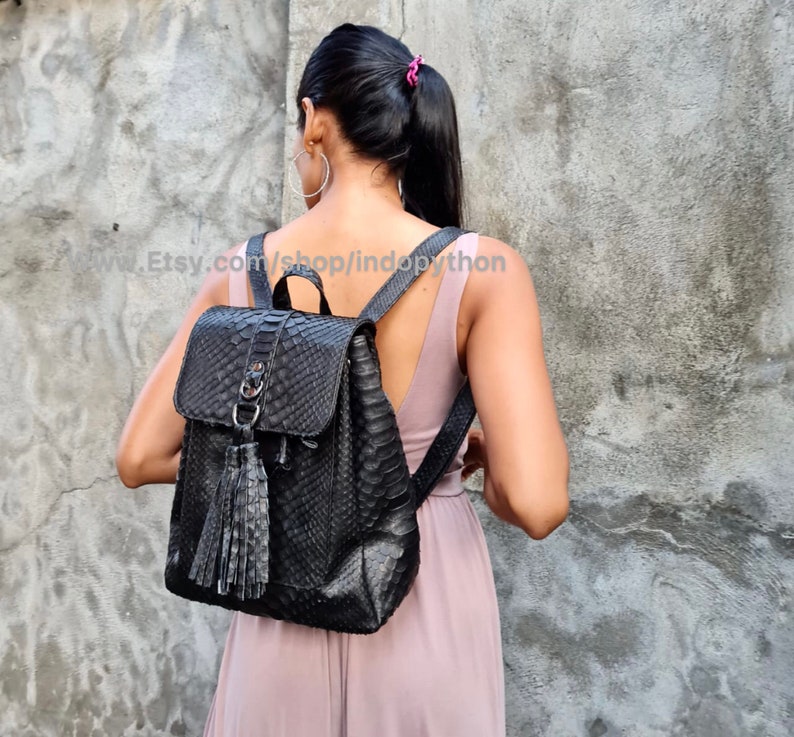 May include: A black leather backpack with a snakeskin pattern and a tassel. The backpack has a zip closure and adjustable straps.