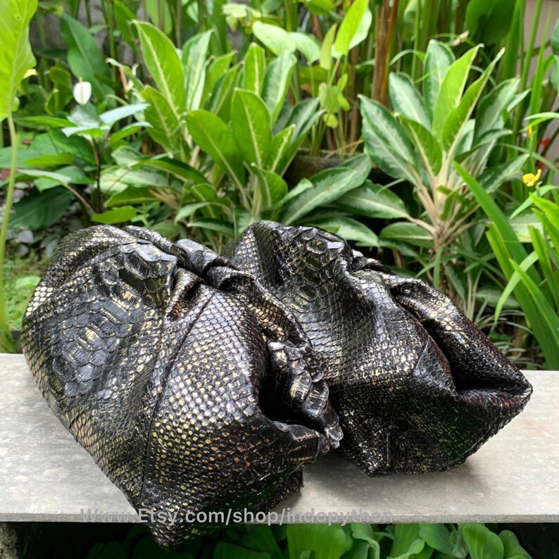K&ouml;nnte beinhalten: Zwei schwarze und goldene Clutch-Taschen aus Pythonleder. Die Taschen sind aus weichem, geschmeidigem Leder gefertigt und haben ein einzigartiges, strukturiertes Design.