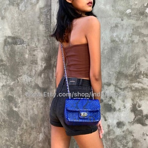 May include: A small blue snakeskin handbag with a silver chain strap. The bag has a flap closure with a silver clasp.