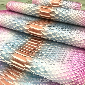 Op de afbeelding: Stapel van iriserende slangenhuid in tinten roze, blauw en wit. Het leer heeft een textuur met schubben.