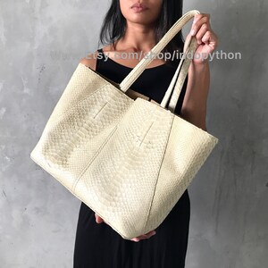 May include: A large off-white tote bag made of python skin. The bag has two top handles and a roomy interior.
