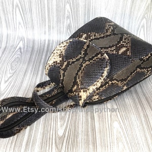 Pu&ograve; includere: Una piccola borsa a mano in pelle di serpente nera e marrone con chiusura a zip e tracolla. La borsa ha una patta con chiusura a zip. La borsa &egrave; su una superficie di legno. www.Etsy.com/shop/SnappyPython
