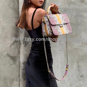 May include: A pink, yellow, and white snakeskin handbag with a silver chain strap. The bag has a top handle and a flap closure with a gold clasp.