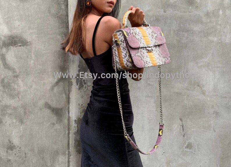 May include: A pink, yellow, and white snakeskin handbag with a silver chain strap. The bag has a top handle and a flap closure with a gold clasp.