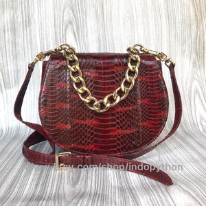 May include: A red snakeskin handbag with a gold chain strap. The bag has a rounded shape and a flap closure.