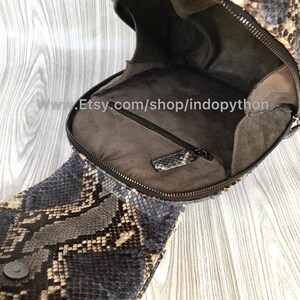 Pu&ograve; includere: Uno zaino in pelle di serpente marrone e nero con chiusura a zip. Lo zaino &egrave; aperto e l'interno &egrave; rivestito in tessuto marrone. Lo zaino ha una piccola tasca all'interno.