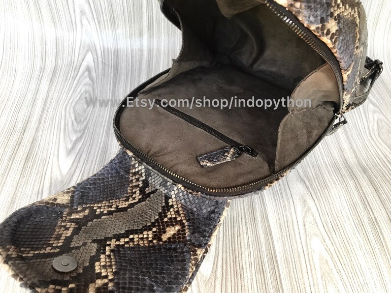 Pu&ograve; includere: Uno zaino in pelle di serpente marrone e nero con chiusura a zip. Lo zaino &egrave; aperto e l'interno &egrave; rivestito in tessuto marrone. Lo zaino ha una piccola tasca all'interno.