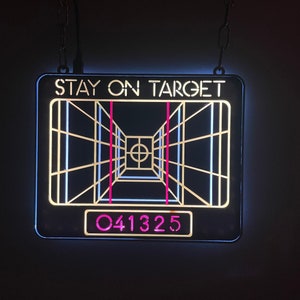 May include: A black and white sign with the text "STAY ON TARGET" and a graphic of a targeting system with a red and white target. The sign also has the number "041325" in pink.