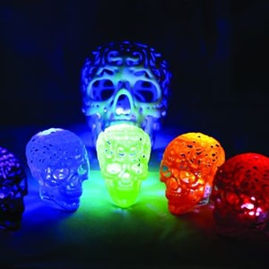 Pu&ograve; includere: Sette piccole figurine di teschio luminose, dal design intricato, in vari colori, tra cui viola, blu, verde, arancione e rosso, disposte su una superficie scura.