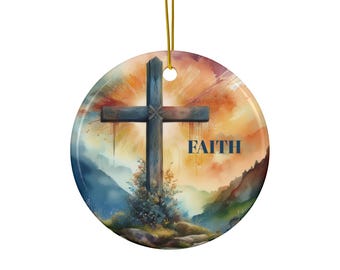 Op de afbeelding: Ronde keramische ornament met een aquarel landschap, een houten kruis en het woord "FAITH". De achtergrond toont een zonsondergang met oranje en gele tinten en een berglandschap.